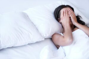 woman in bed going without sleep suffering from insomnia covering eyes with hands - The Fourth